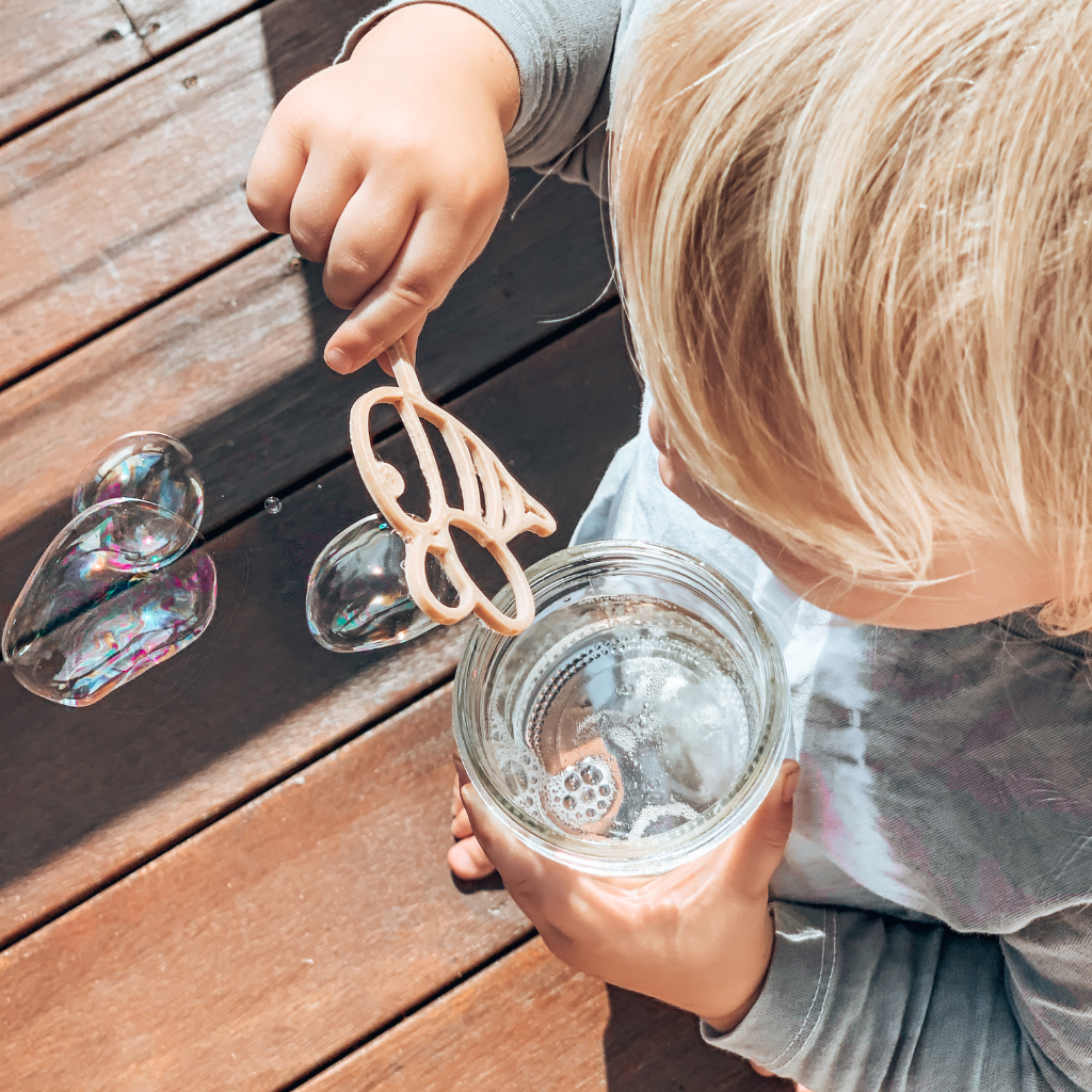 Young child with bee shaped bubble wand blowing bubbles. Australian made, all natural bubble wand which is biodegradable. Spark your child’s imagination with nature toys.