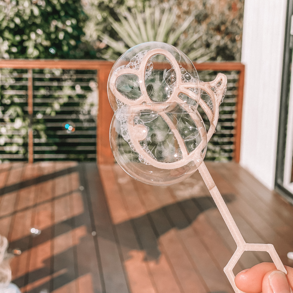 Young child with bee shaped bubble wand blowing bubbles. Australian made, all natural bubble wand which is biodegradable. Spark your child’s imagination with nature toys.