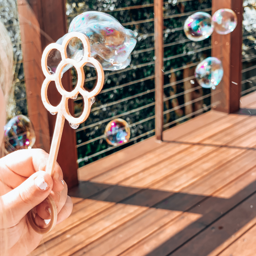 Young child with flower shaped bubble wand blowing bubbles. Australian made, all natural bubble wand which is biodegradable. Spark your child’s imagination with nature toys.