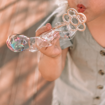 Young child with flower shaped bubble wand blowing bubbles. Australian made, all natural bubble wand which is biodegradable. Spark your child’s imagination with nature toys. from Kinfolk Pantry.