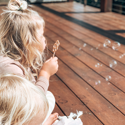 Young child with flower shaped bubble wand blowing bubbles. Australian made, all natural bubble wand which is biodegradable. Spark your child’s imagination with nature toys from Kinfolk Pantry.