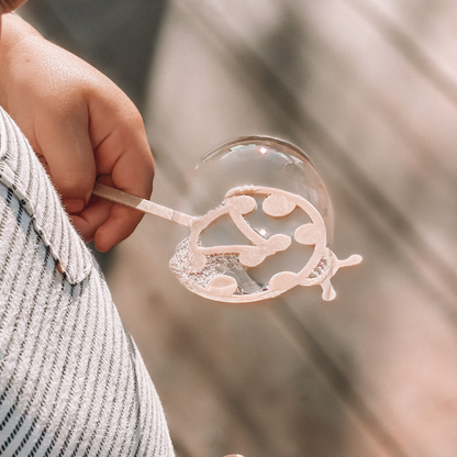 Young child with ladybird shaped bubble wand blowing bubbles. Australian made, all natural bubble wand which is biodegradable. From Kinfolk Pantry.